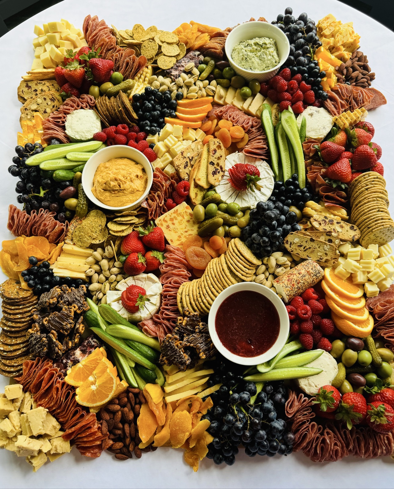 Overhead view of a grazing board with meats, cheeses, fruit, crackers and dips
