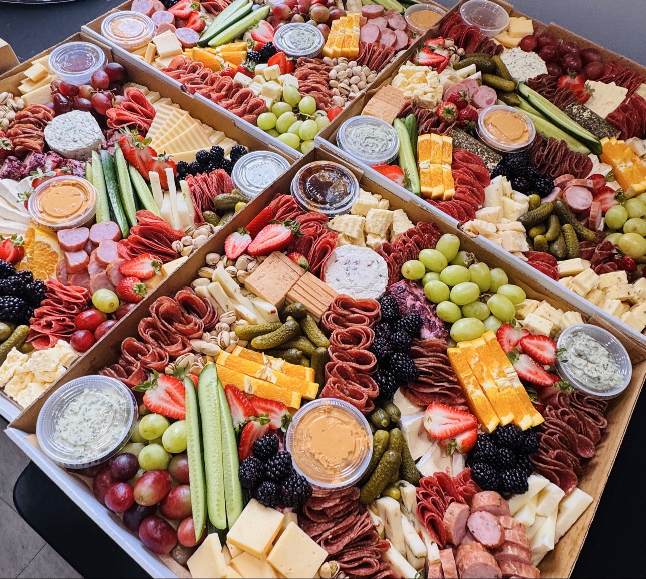 Four open charcuterie boxes filled with meats, cheeses, fruit and accompaniments